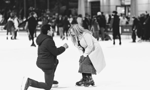 a man on a ice rink is down on one knee asking his girlfriend to marry him as she screams with excitement