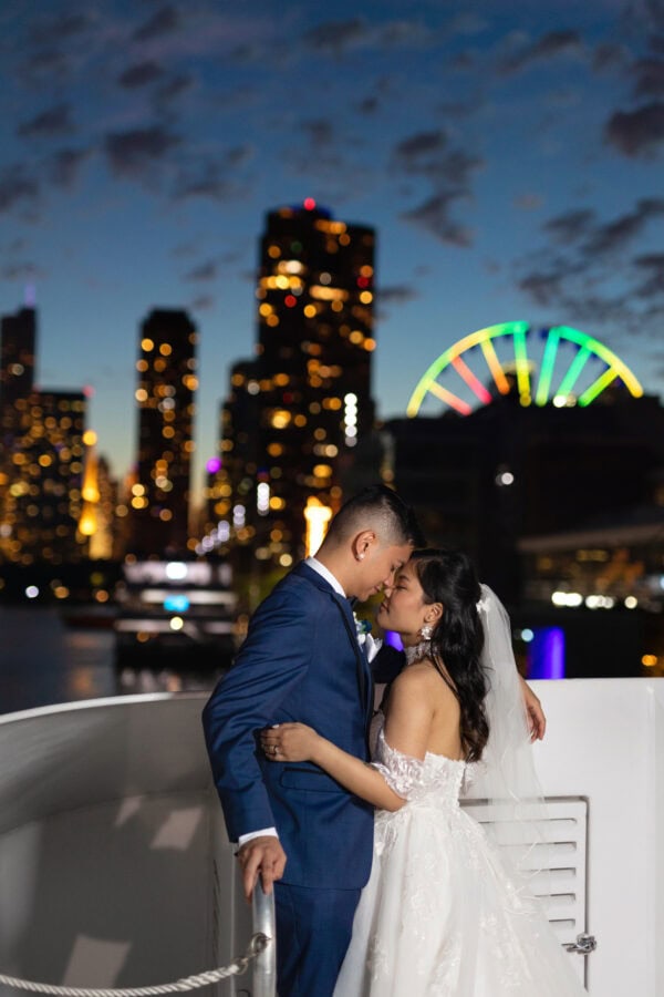 bride an groom looking into each others eyes while standing on a boat in front of the chicago night skyline