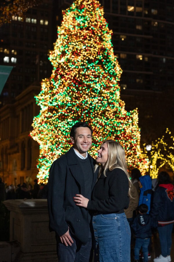 engaged couple poses for a photo in front of lit christmas tree in millennium park