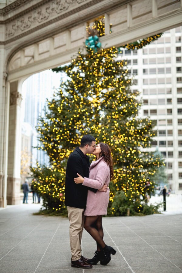 engaged couple poses for a photo in front of a christmas tree at the wrigley building chicago